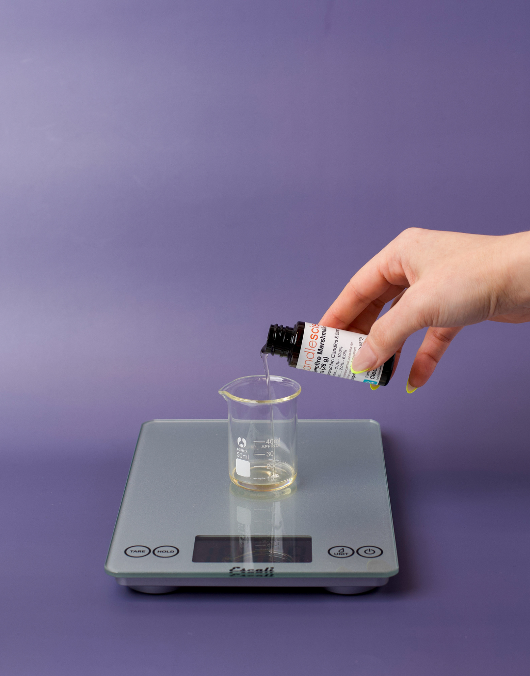 Pouring fragrance oil into glass beaker on scale.